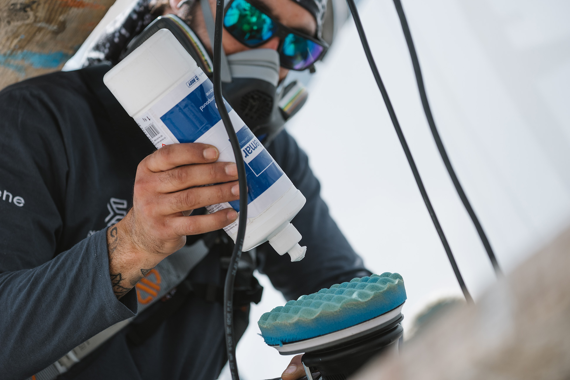 Στιγμιότυπο από εταιρική φωτογράφιση για την Exceptional Yachting, με τεχνικό προσωπικό σε πλήρη εξοπλισμό να προετοιμάζει εργαλείο γυαλίσματος, αναδεικνύοντας την τεχνική αρτιότητα και την προσοχή στη λεπτομέρεια στη φροντίδα πολυτελών σκαφών.